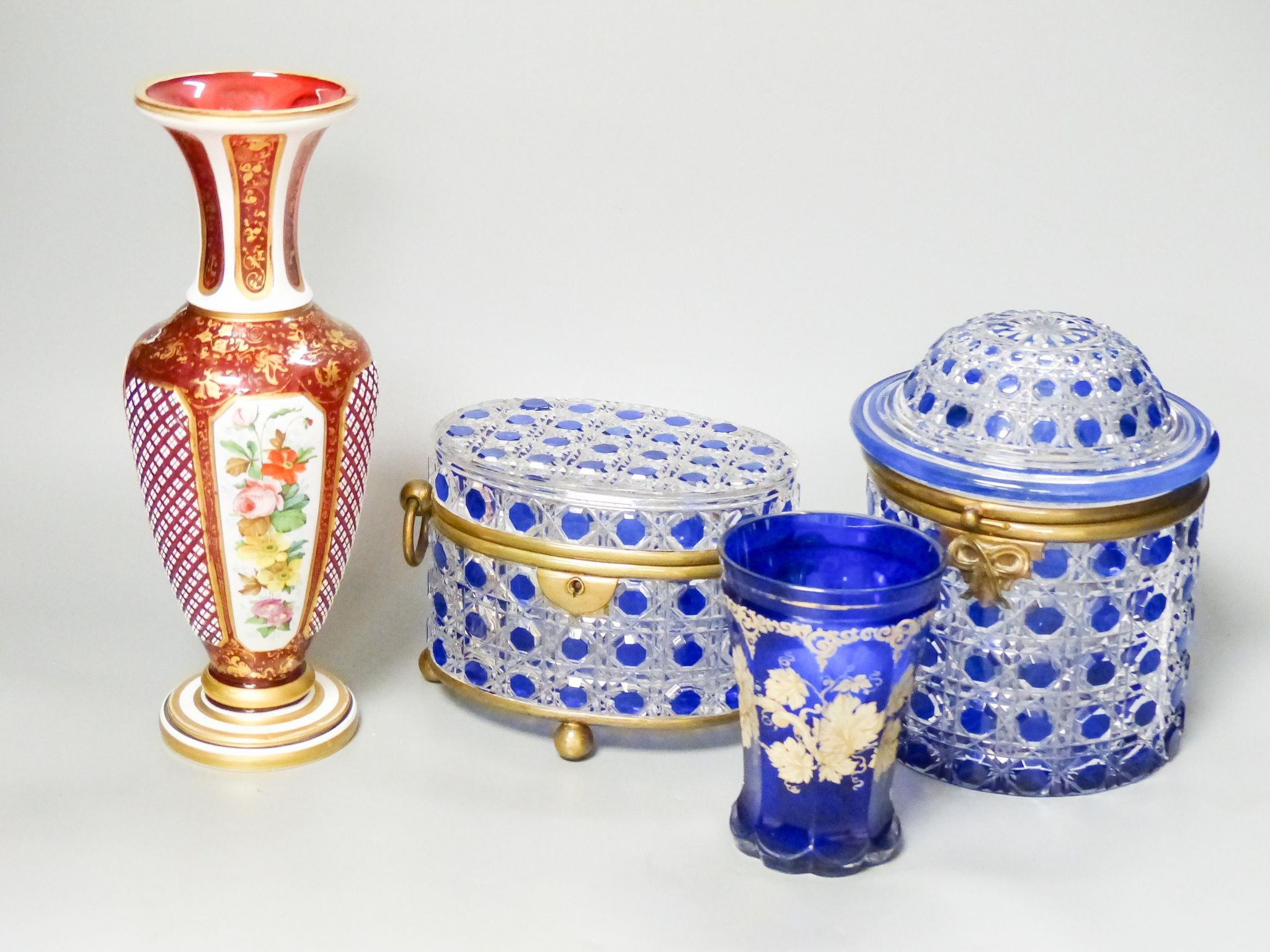 A 19th century Bohemian overlaid glass vase, 25.5cm, a similar gilded and enamelled beaker and two blue flashed hobnail glass biscuit boxes and covers